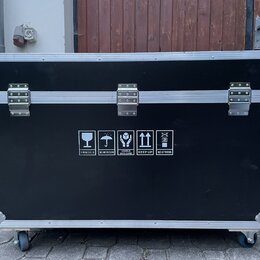 Černý transportní flightcase s hliníkovými hranami a kovovými rohy. Přední strana obsahuje tři stříbrné zapínací zámky a bílé informační piktogramy s…