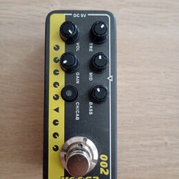 Černý efekt pedál s žlutým pruhem na levé straně. Na horní části jsou pět regulačních knoflíků s popisky VOL, TRE, GAIN, MID a BASS, dále tlačítko CH…