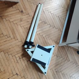 Bílý rozkládací stojan s dvěma teleskopickými trubicemi. Na spodní části je viditelný nápis Millennium a malá bílá nálepka s čárovým kódem. Povrch je…