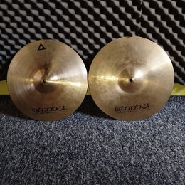Dvě mosazné činely s viditelným opracováním povrchu. Oba mají v dolní části nápis istanbul Agop Made in Turkey. Levý činel má navíc v horní části tro…