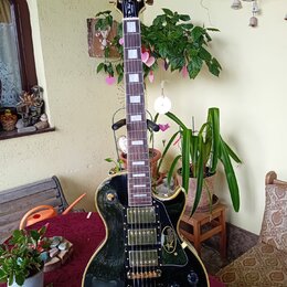 Černá elektrická kytara typu Les Paul se zlatým hardwarem a bílými vložkami na hmatníku. Na hlavě je nápis Gibson a logo s hvězdou, na hmatníku je u…