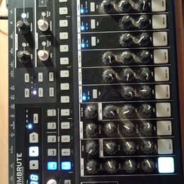 Černý analogový syntezátor s dřevěným rámem. Na zařízení je nápis DRUMBRUTE ANALOG DRUM SYNTHESIZER a logo ARTURIA s textem YOUR EXPERIENCE SOUND. Př…