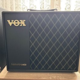 Černý kytarový kombo zesilovač s pravou stranou pokrytou látkou s bílým kosočtvercovým vzorem. V horní levé části je umístěno zlaté logo VOX a v doln…
