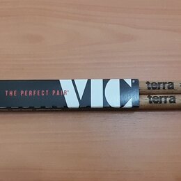Dvě dřevěné bubenícké paličky s bílými hroty. Na obou je černý nápis terra 7AN. Paličky jsou v originálním papírovém obalu s nápisy THE PERFECT PAIR®…
