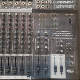 Šedý 12kanálový mixážní pult s nápisy PEAVEY, UNITY SERIES a 2002-12 RQ. Na přístroji je text 12 CHANNEL PROFESSIONAL STEREO CONSOLE a v pravém dolní…