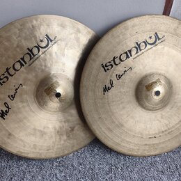 Dvě mosazné činely s viditelným broušením povrchu. Oba mají černý nápis istanbul a menší text Handmade cymbals from Turkey. Pod hlavním logem je na o…
