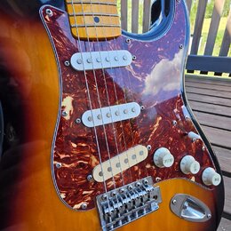 Elektrická kytara s trupem v barevném přechodu od žluté přes oranžovou k hnědé. Nástroj má hnedý mramorovaný pickguard, tři bílé snímače a javorový h…