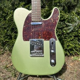 Elektrická kytara typu Telecaster v olivově zelené metalické barvě s hnědo-červeným vzorovaným pickguardem. Nástroj má javorový hmatník a chromované…