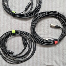 Tři srolovaný černé audio kabely. Dva z nich mají koncovky typu XLR, jeden má jednu koncovku typu jack. Kabely jsou stahovány barevnými suchými staho…