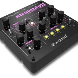Černý string syntetizér s nápisem streichfett STRING SYNTHESIZER a logem waldorf. Přístroj má mnoho černých ovládacích knoflíků, přepínačů a čtyři žl…