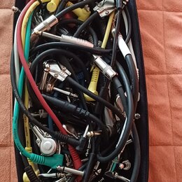 Černý oválný pouzdro obsahuje množství různých audio kabelů v barvách černé, žluté, červené a tyrkysové. Kabely mají různé typy konektorů, včetně jac…