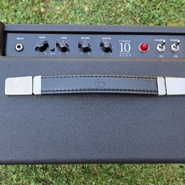 Kytarový kombozesilovač v černém texturovaném potahu s černým ovládacím panelem. Na panelu jsou nápisy INPUT, GAIN, TONE, REVERB, MASTER, STUDIO 10 E…