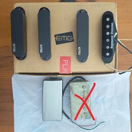 Na kartonové krabici s logem EMG leží čtyři snímače k elektrické kytáře. Tři z nich jsou černé s nápisem EMG a jeden je černý s nápisem Seymour Dunca…