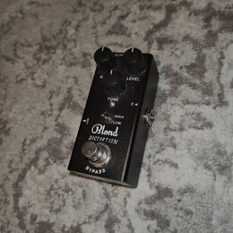 Černý efekt pedál s nápisy Blond a DISTORTION. Na horní straně jsou tři ovládací knoflíky s popisky G, LEVEL a TONE, přepínač HIGH/LOW a vstup pro na…