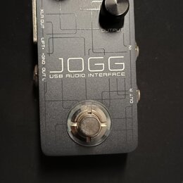 Šedý obdélníkový USB audio interface s kovovým povrchem. Na horní straně jsou dva černé ovládací knoflíky s popisky GAIN a OUTPUT a logo HOTONE. Upro…