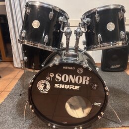Černá bicí souprava tvořená dvěma tommy a basovým bubnem. Na basovém bubnu jsou viditelné nápisy SONOR, SHURE, METALO a bern, dále logo National Drum…