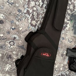 Černý polotvrdý pouzdro (gig bag) na hudební nástroj s dlouhým úzkým tvarem. Na přední kapsi je umístěno červenobílé logo SKB. Pouzdro má připevněný…