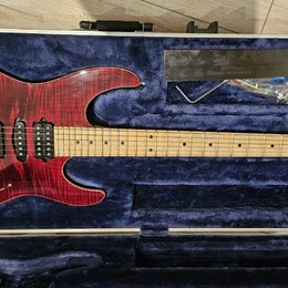 Elektrická kytara s červeným plamenovitým povrchem korpusu a světle hnědým hnedem hmatníkem. Na hlavě je bílý nápis "Schecter". Nástroj má tři snímač…