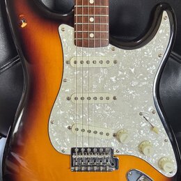 Elektrická kytara s korpusem v barevném přechodu od tmavě hnědé k žluté. Nástroj má bílý perleťový pickguard, tři snímače s bílými plastovými kryty a…