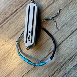 Bílý humbucker s dvěma černými polosnovými kryty snímačů. Na spodní části je svisle napsáno logo DiMarzio. Snímač má připojovací kabely v různých bar…
