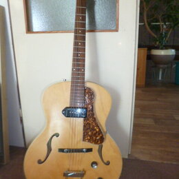 Polodupatá elektrická kytara s přírodním dřevěným povrchem a dvěma f-otvory. Na hlavě je viditelné logo značky Epiphone. Kytara má jeden snímač u krk…