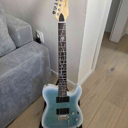 Elektrická kytara s modrým přechodovým povrchem těla a hnědým hmatníkem. Na hlavě je viditelné logo Fender. Hmatník obsahuje bílé dekorativní vložky…