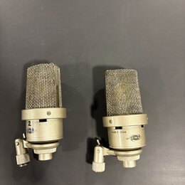 Dva kondenzátorové mikrofony stříbrné barvy s kovovými mřížkami. Na těle pravého mikrofonu je nápis -10dB 0 20dB a logo NEUMANN. Levý mikrofon má na…
