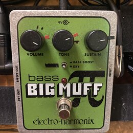 Zelený efekt pedál s kovovým rámem. Na povrchu jsou tři černé ovládací knoflíky s popisky VOLUME, TONE a SUSTAIN, přepínač s nápisy BASS BOOST a DRY…