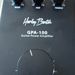 Černý kytarový výkonový zesilovač s nápisy Harley Benton, GPA-100 a Guitar Power Amplifier. Horní část obsahuje tři menší otočné ovladače s popisky B…