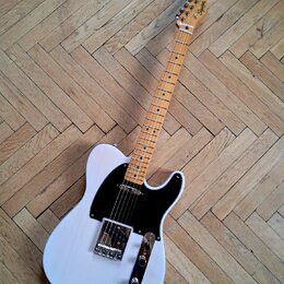 Bílá elektrická kytara typu Telecaster s černým pickguardem a hnedým javorovým hmatníkem. Na hlavě krku je viditelné logo "Squier". Nástroj vykazuje…