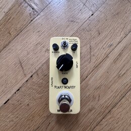 Krémový efekt pedál s nápisy FUNKY MONKEY a MOOG. Na horní straně jsou ovládací prvky: dva malé černé knoflíky u nápisů RANGE a Q, jeden velký černý…