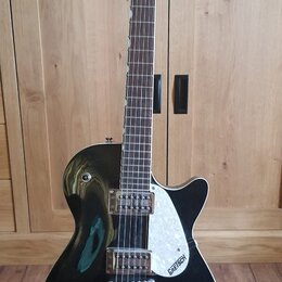 Černá elektrická kytara s tmavým hmatníkem a bílým trsátorem. Na hlavě i na trsátoru je bílý nápis GRETSCH. Nástroj má dva snímače typu humbucker a j…