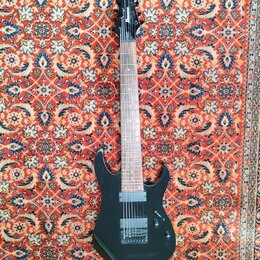 Černá elektrická kytara s tmavým hnedým hmatníkem. Na hlavě je bílý nápis Ibanez. Nástroj má dva humbuckery, jeden ovládací knoflík a přepínač. Povrc…