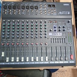 Šedý mixážní pult značky YAMAHA, model MX12/4. Zařízení obsahuje několik vstupních kanálů s posuvníky, knoflíky pro gain a ekvalizaci a sekci ST GRAP…
