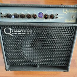 Černý basový kombozesilovač s kovovou mřížkou reproduktoru. Na předním panelu je nápis HUGHES & KETTNER QUANTUM BASS TECHNOLOGY a označení modelu QC…