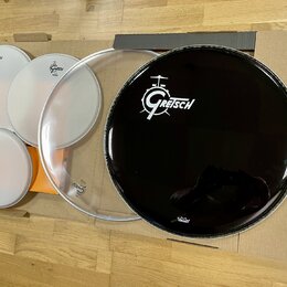Sada bubenových koží položená na kartonovém podkladu. Na bílých a průhledné kožem jsou viditelná loga Gretsch. Největší černá koža nese bílé logo Gre…