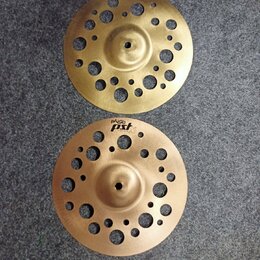 Dvě mosazné činely s perforací v podobě otvorů různých velikostí. Oba mají v horní části černý nápis paiste PST. Povrch je matný s viditelnými stopam…