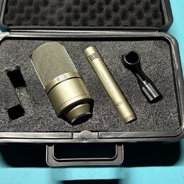 Černý tvrdý kufřík s pěnovou výplní obsahuje zlatavý mikrofon a dopřívodní příslušenství. Na těle mikrofonu je nápis "Cardioid Microphone 991" a logo…