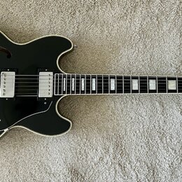 Černá polodupatá elektrická kytara s bílým lemováním a hnědými f-otvory. Na hlavě je viditelné logo Gibson. Nástroj má dva humbuckery, tři ovládací k…