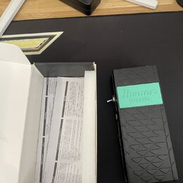 Černý efekt pedál s výrazným texturovaným povrchem v horní a dolní části. Uprostřed je tyrkysový obdélník s nápisem Ibanez WH10. Vedle pedálu je otev…