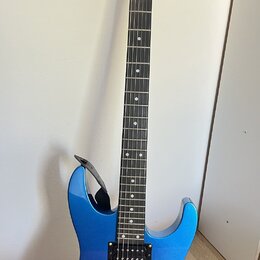 Modře lakovaná elektrická kytara s černým hmatníkem a černými hardwarem. Na hlavě je bílý nápis Jackson. Nástroj má dva humbuckery, jeden ovládací kn…