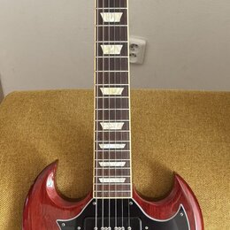 Elektrická kytara s červeným lakem a černým pickguardem. Na hlavě hmatníku je bílý nápis Gibson a na spodní části nápis Standard. Kytara má dva humbu…