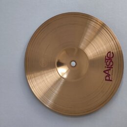 Kruhový činel z mosazného kovu s jemným rýhováním. Na povrchu je vpravo viditelné červené logo Paiste a pod ním menší nápis MADE IN SWITZERLAND. Povr…