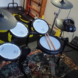 Elektronická bicí souprava značky Roland s bílými padovými plochami a černými činely. Na padech jsou viditelné nápisy Roland a V-Drums. Součástí je č…