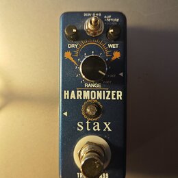 Modrý efekt pedál s nápisy HARMONIZER a stax. Na horní části jsou dva černé otočné knoflíky s popisky DRY a WET, centrální knoflík s rozsahovou stupn…