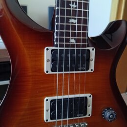 Elektrická kytara s hnědým lakovaným povrchem s viditelnou strukturou dřeva. Nástroj má dva snímače typu humbucker s bílými rámečky, na kterých je uv…