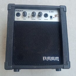 Černý malý kytarový kombo zesilovač s bílým ovládacím panelem. Na panelu jsou nápisy REEF AUDIO, LA5, INPUT, GAIN, VOLUME, TONE, PHONES a DC9V. Na sp…