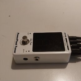 Bílý kytarový pedál s nápisem PowerPlant Tuner a logem Harley Benton. Zařízení má stříbrný spínač s nápisem True Bypass, displej a konektory IN a OUT…