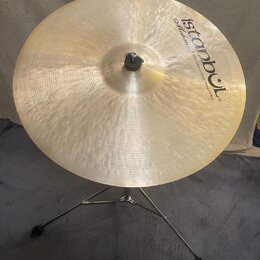 Zlatavý kovový činel umístěný na chromovaném stojanu. Na povrchu je černý nápis „Istanbul“ s hvězdicí a pod ním menší text „Mehmet Handmade Cymbals f…