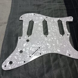 Bílý pickguard s perleťovým efektem určený pro elektrickou kytaru. Povrch je hladký a reflexní, bez viditelných značek, log nebo nápisů. Kousek vykaz…